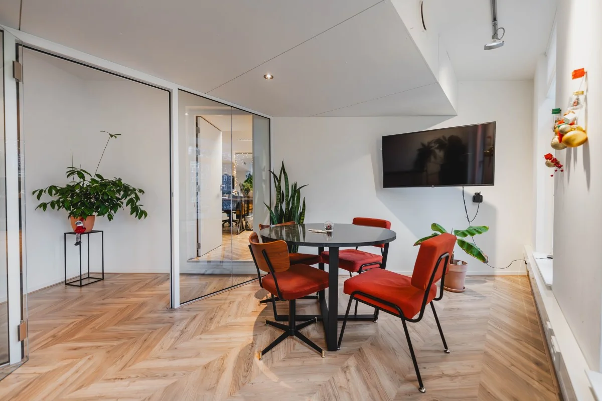 Moderne vergaderruimte aan de Korte Reguliersdwarsstraat met ronde tafel, rode stoelen, planten en een muurtelevisie.